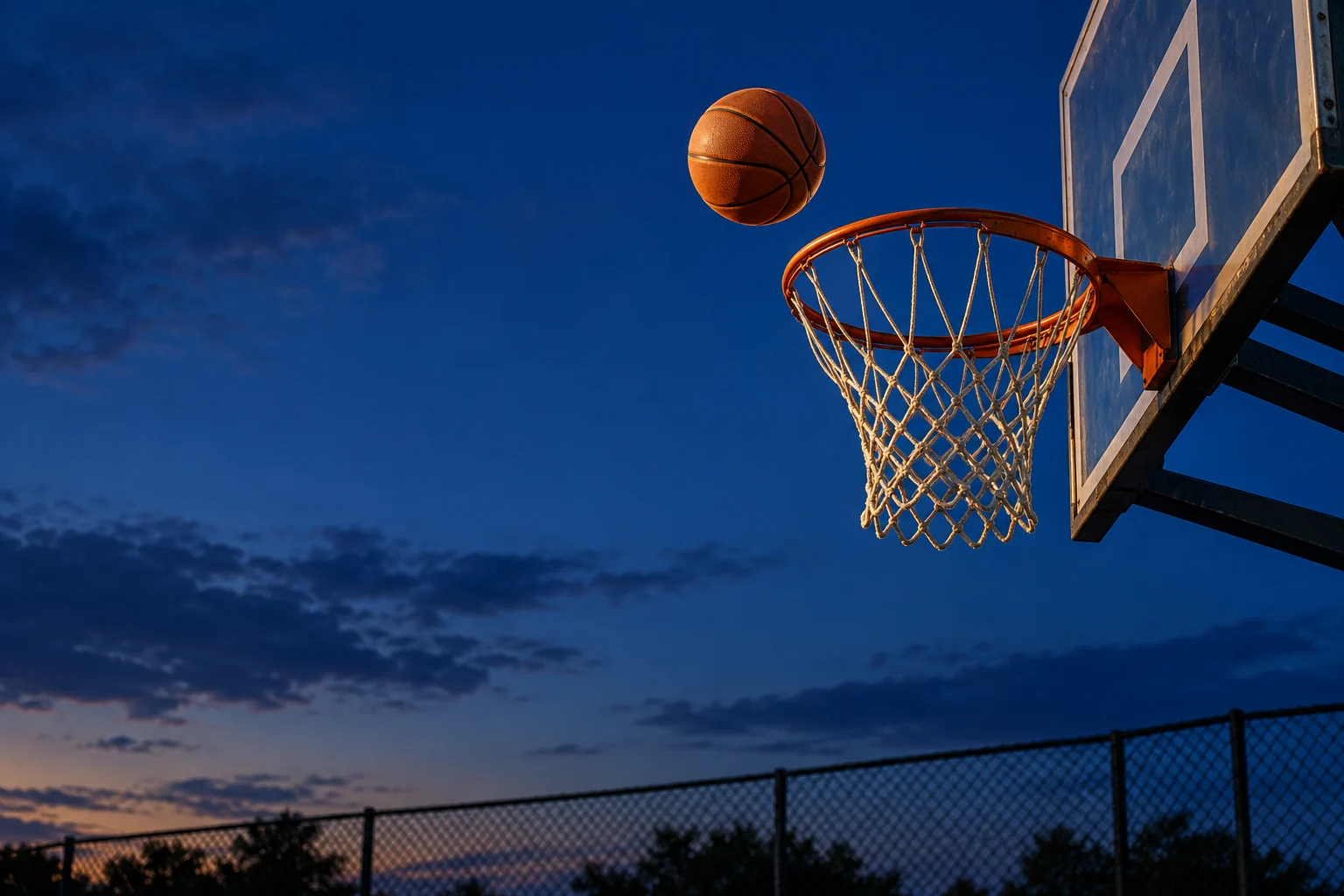A basketball approaching an outdoor hoop against an evening sky
